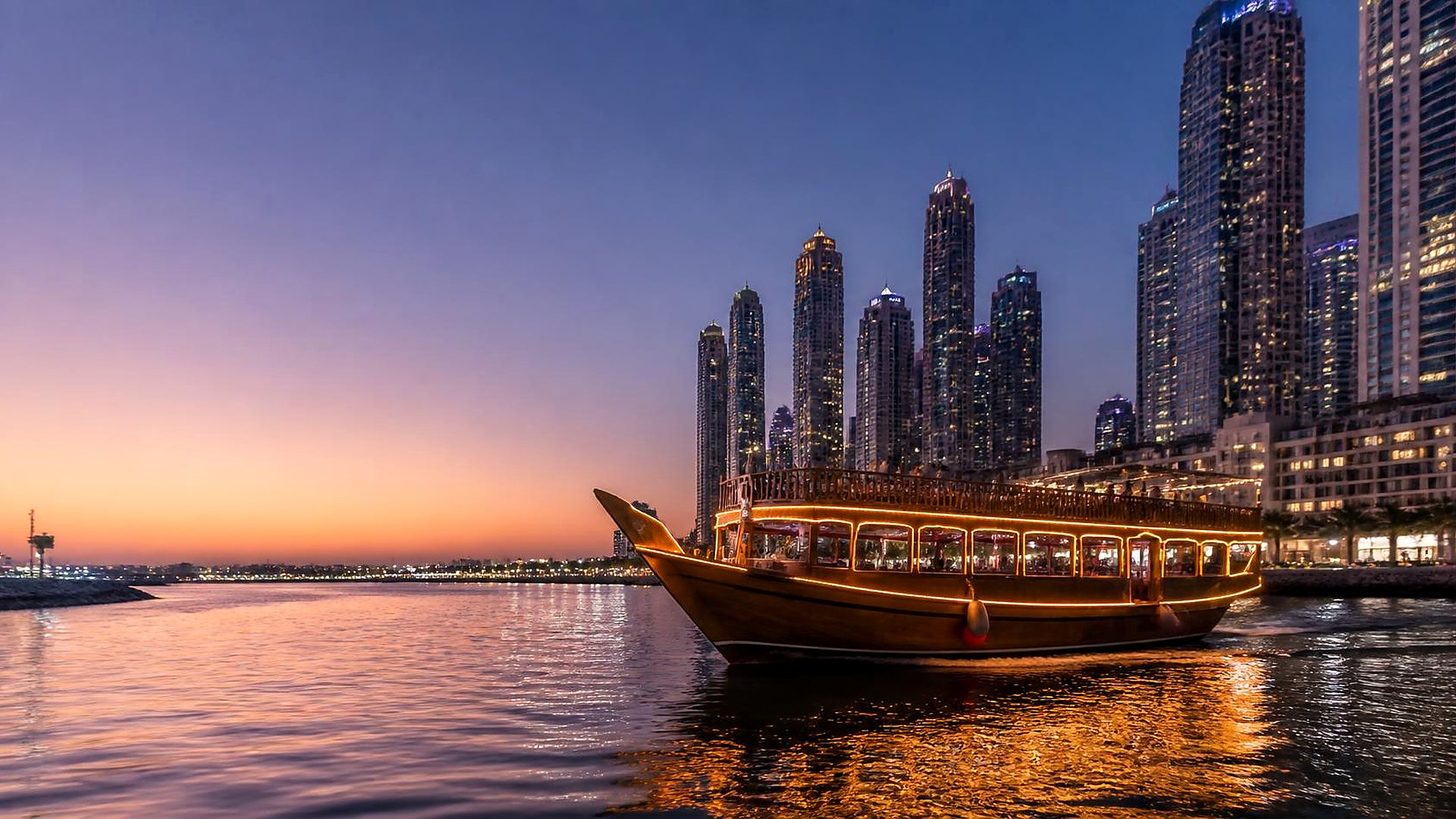 Illuminated wooden dhow in front of the Dubai Marina towers at dusk