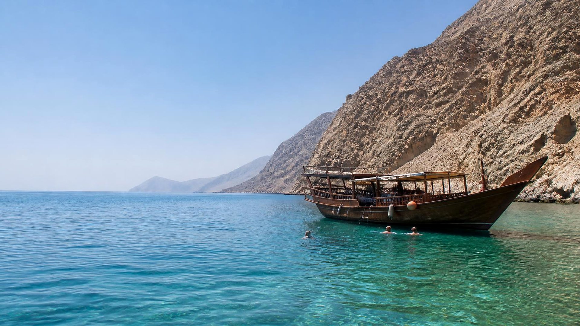 Traditional dhow in a turquoise bay below the cliffs of Musandam