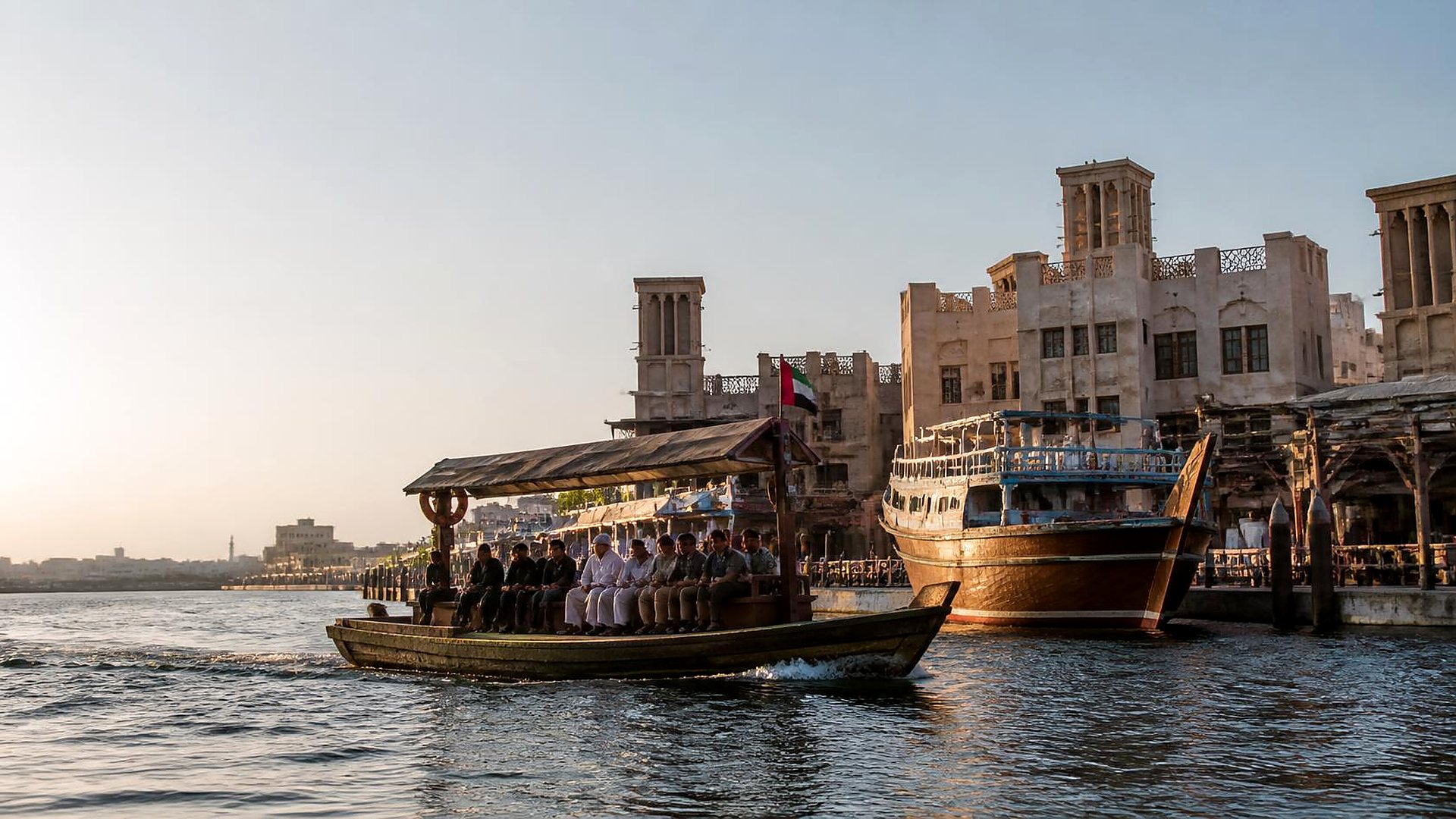 Abra boat with passengers crossing Dubai Creek in front of wind towers