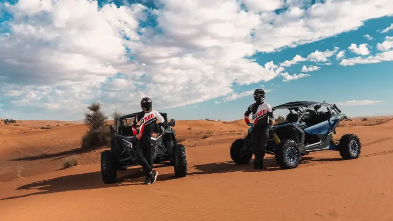 Two drivers in helmets beside their buggies in the desert