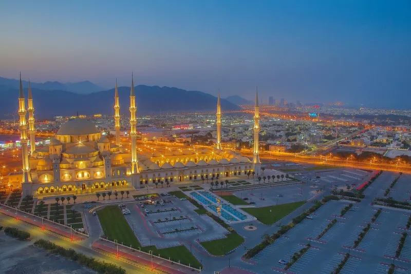 Sheikh Zayed Mosque in Fujairah lit up at dusk below the Hajar Mountains