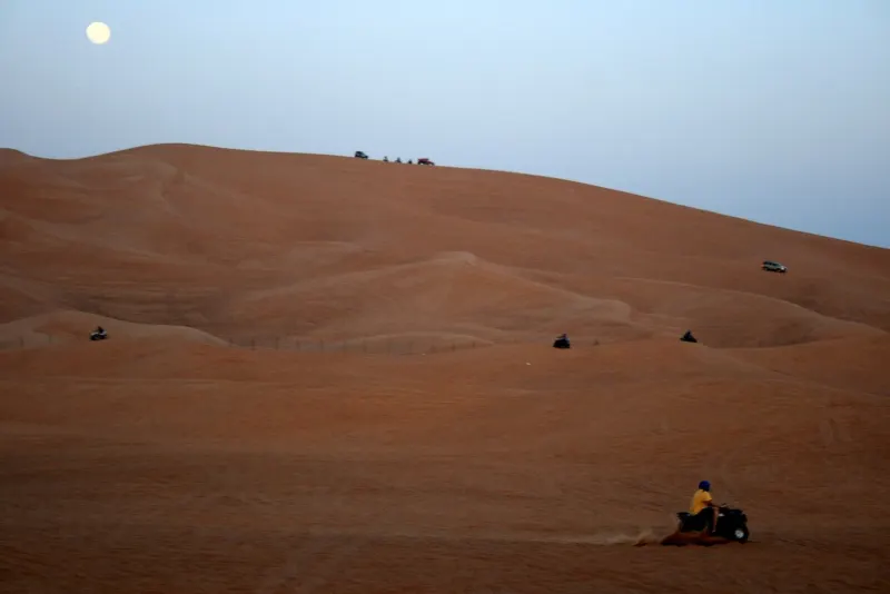 Quad bike rider on a large dune in the Dubai desert at dusk