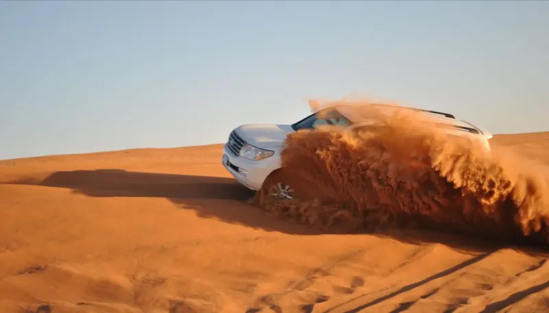White 4x4 throwing up sand on a dune drive